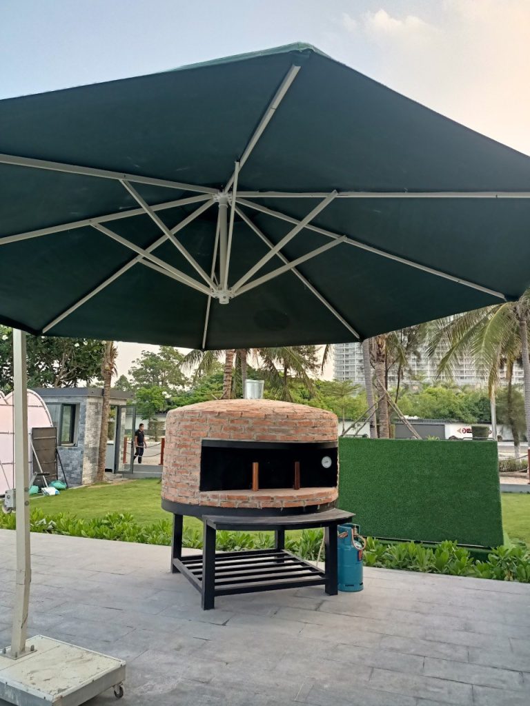 Lò pizza Napoli 1500 đặt dưới dù trong sân vườn, ảnh thật